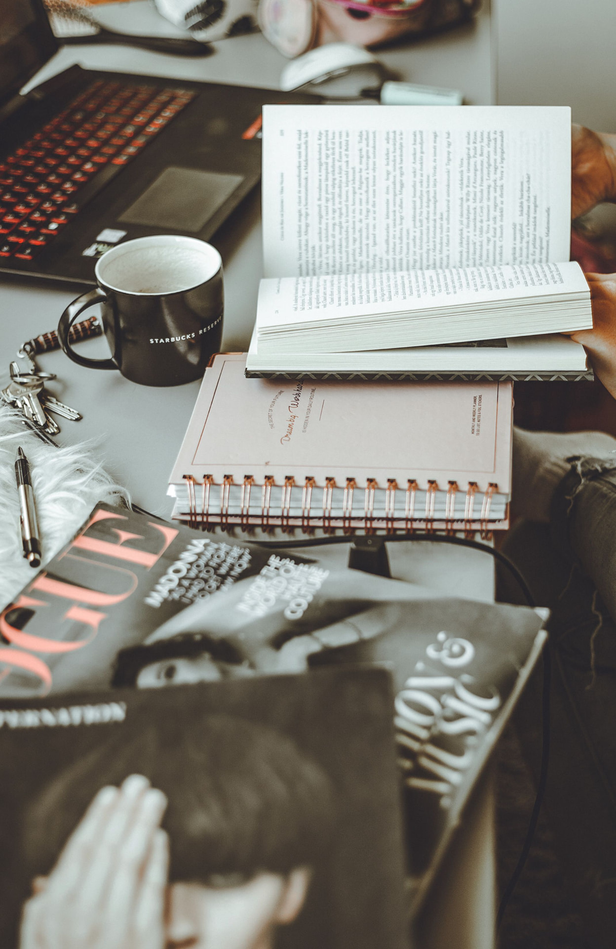 A desk stacked with books, planners, and a coffee mug